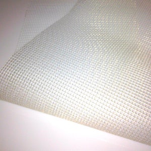 May include: Close-up of a section of white, square-patterned mesh fabric. The mesh is tightly woven, creating a grid-like texture. The fabric appears to be lightweight and slightly translucent, with a subtle sheen. The overall appearance is clean and simple.