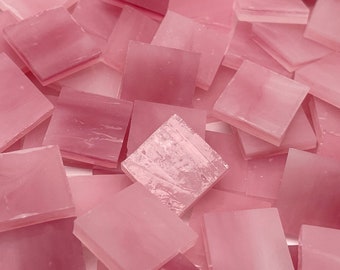 May include: A pile of pink glass mosaic tiles. The tiles are square and have a translucent, iridescent finish.