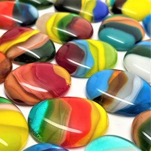 May include: A collection of colorful, oval-shaped glass stones. Each stone features a unique blend of vibrant colors, including red, yellow, green, blue, and orange, swirled together to create a marbled effect. The stones are smooth and glossy.