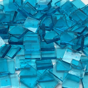 May include: A pile of turquoise blue glass tiles. The tiles are square and have a smooth, glossy finish.
