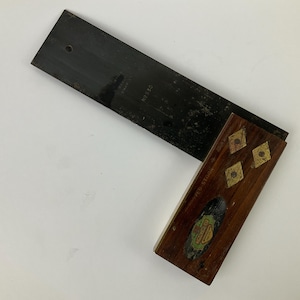 May include: A vintage carpenter's square with a black metal blade and a wooden handle. The handle is dark brown with inlaid diamond shapes and a label. The blade has the number "N9530" printed on it.