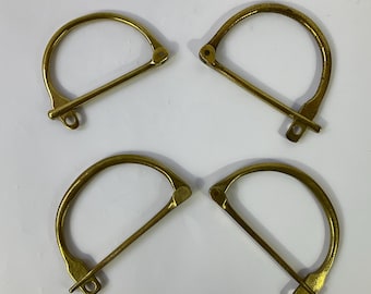 Puede incluir: Cuatro grilletes en forma de D de color latón. Cada grillete tiene una parte superior curvada y un pasador recto que se desliza a través del anillo. Los grilletes están dispuestos en forma cuadrada sobre un fondo blanco. Probablemente se utilizan para diversos proyectos de artesanía o ferretería.