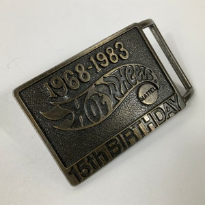 May include: A gold-toned metal belt buckle with the Hot Wheels logo and the text "1968-1983 15th Birthday" and a small Mattel logo.