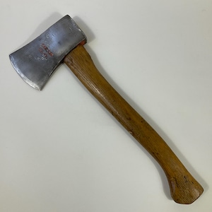 Puede incluir: Un hacha vintage con mango de madera y cabeza plateada. La cabeza del hacha tiene el texto "SABRE SAW U.S.A." en letras rojas. El mango es de color marrón claro y tiene forma curva.