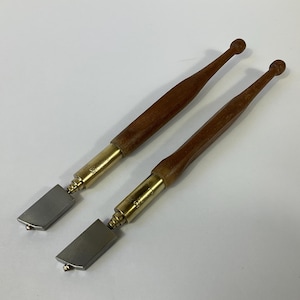 May include: Two glass cutters. Each has a wooden handle, brass fittings, and a rectangular silver blade. The handles are dark brown and have a rounded end. The tools are for cutting glass.