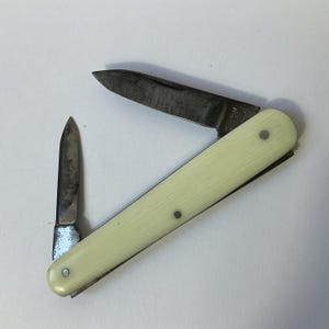 May include: A small, two-bladed pocket knife with a white plastic handle. The blades are closed and the knife is in a closed position.
