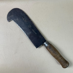 May include: A vintage, metal, hand-forged,  curved blade with a wooden handle. The blade has the text "A.F.G.  MADE IN GERMANY" etched into the metal.