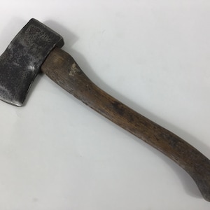May include: A vintage axe with a wooden handle. The axe head is made of metal and has a dull finish. The handle is brown and has a slight curve at the end.