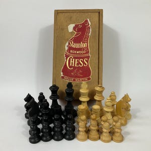 Pode incluir: Um conjunto de xadrez de madeira vintage com peças pretas e brancas numa caixa de madeira. A caixa tem um rótulo que diz "Staunton Boxwood Chess House Martin".