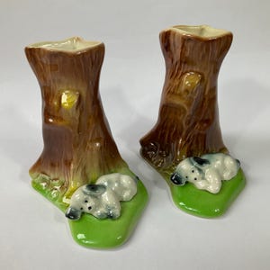 May include: A pair of brown ceramic tree stump vases with a sleeping dog at the base of each. The vases are glazed in a brown and green colour scheme.
