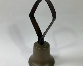 May include: A vintage brass bell with a dark metal handle. The handle is shaped like a diamond and is attached to the top of the bell.