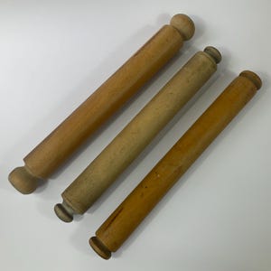 Può includere: Tre mattarelli in legno di diverse tonalità di marrone. Ogni mattarello ha un corpo cilindrico e manici arrotondati. La venatura del legno è visibile. I mattarelli sono lunghi circa 30 cm.