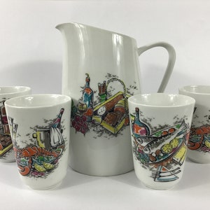 May include: A set of four white ceramic mugs with a colorful picnic scene design, including a lobster, fish, wine bottles, and bread. The set also includes a matching white ceramic pitcher with the same design.