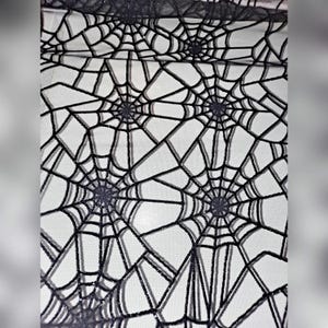 May include: A sheer black fabric featuring a repeating spider web pattern. The web design is rendered in a dark, textured material that contrasts against the translucent mesh background, creating a distinct geometric grid of interconnected lines.