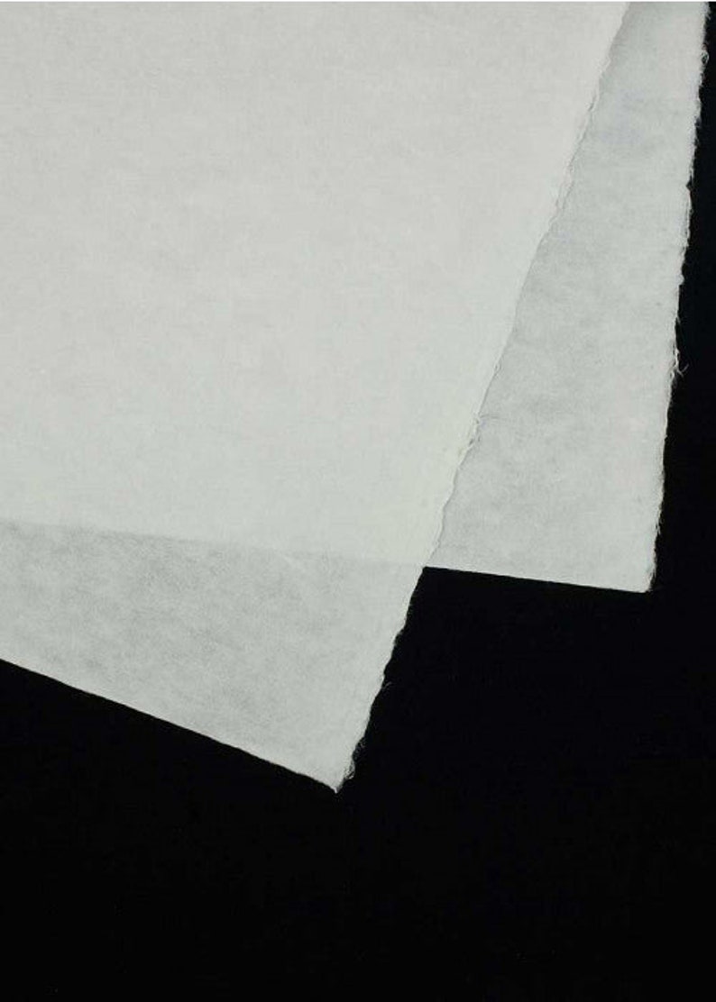 Może przedstawiać: Zbliżenie na biały, teksturowany arkusz papieru o lekko szorstkiej powierzchni. Papier jest złożony na p&oacute;ł, tworząc fałdę w środku. Papier znajduje się na czarnym tle.