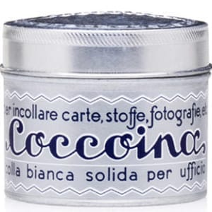 Può includere: Un piccolo barattolo argentato di colla Coccolina. Il barattolo ha un coperchio argentato e un'etichetta bianca con testo blu. L'etichetta recita "Coccolina" in corsivo, con testo aggiuntivo in italiano. La colla è descritta come bianca e solida.
