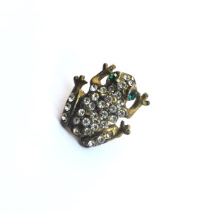 May include: A gold-toned frog brooch with clear rhinestones and green eyes.