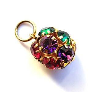 May include: A gold charm with a round, multi-faceted design. The charm is adorned with red, green, and purple rhinestones.