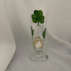 May include: A clear glass beer stein with a hand-painted design of green four-leaf clovers and a white clover.