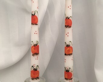 Könnte beinhalten: Zwei weiße Kerzen mit handbemalten orangefarbenen Kürbissen und roten Punkten. Die Kerzen stehen in gläsernen Kerzenhaltern.