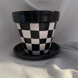 May include: Black and white checkered terracotta planter with a matching saucer. The planter has a black rim and a white base.