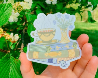 May include: A sticker featuring a vintage illustration of a cup of tea, a vase of flowers, and a stack of books. The sticker is on a white background.