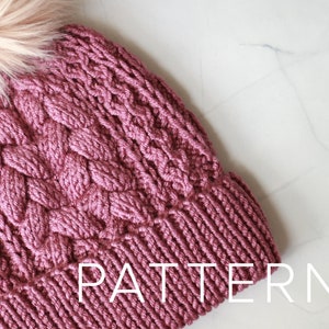 Puede incluir: Un gorro de punto rosa con un pompón esponjoso en la parte superior. El gorro tiene un patrón de punto de cable y el texto "PATTERN" es visible en la parte inferior de la imagen.