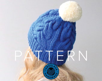 May include: Blue knitted hat with a white pom pom and a cable knit pattern. The hat has the text "PATTERN" in white letters on the front. The hat is worn by a person with blonde hair. The image also includes a blue and white circular logo with the text "YAROSLAVA HANDMADE".
