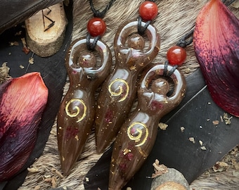 May include: Three brown resin goddess pendants with gold accents and red beads on black cords. The pendants are shaped like a woman's body with a spiral design.