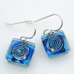 May include: A pair of blue glass earrings with silver hooks. Each earring features a white spiral design with gold accents.