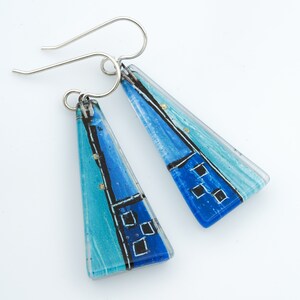 May include: A pair of blue and turquoise glass earrings with silver hooks. The glass is painted with black and white lines and squares.