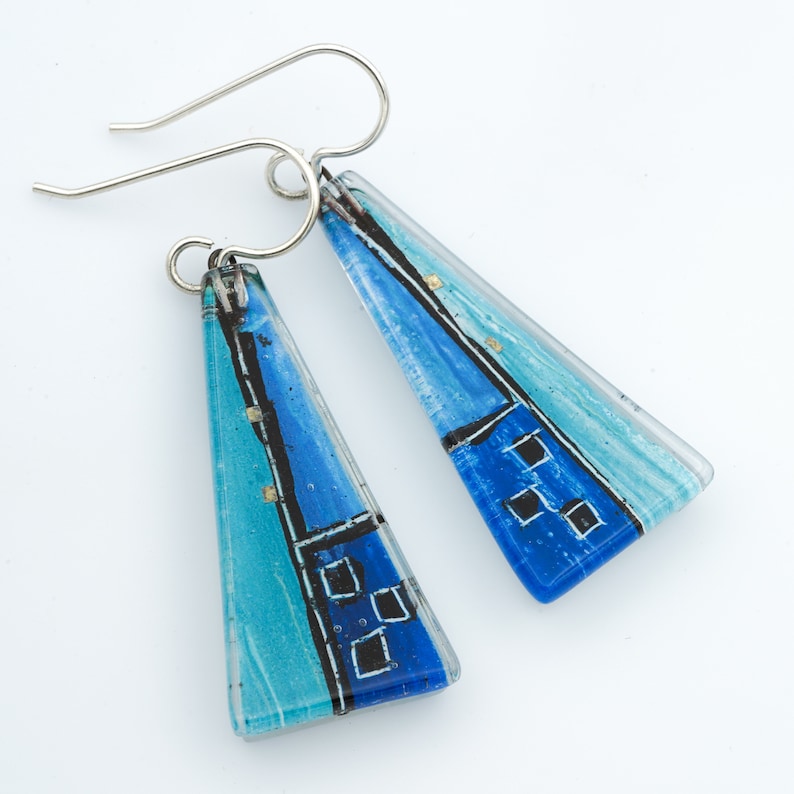 May include: A pair of blue and turquoise glass earrings with silver hooks. The glass is painted with black and white lines and squares.