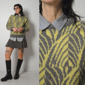 May include: A yellow and gray patterned sweater with a collared shirt underneath, paired with a gray pleated skirt and black knee-high boots. The sweater features a geometric design.