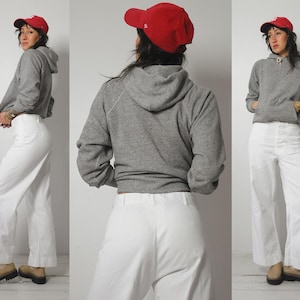 May include: A gray hooded sweatshirt with white pants. The sweatshirt has a drawstring hood and a relaxed fit. The pants are wide-legged and have a high waist.