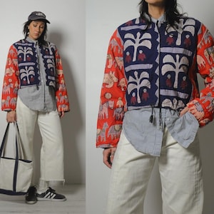 May include: A colorful jacket with a unique design. The jacket features a red background with elephant and figure patterns on the sleeves. The front panels are navy blue with white tree and figure designs. The jacket is worn over a gray and white striped shirt and white pants.