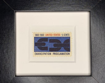 May include: A framed United States postage stamp commemorating the Emancipation Proclamation. The stamp features a blue and black design with the text "1863-1963 UNITED STATES 5 CENTS" and "EMANCIPATION PROCLAMATION".