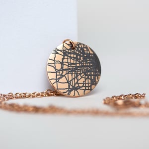 May include: A rose gold necklace with a round pendant featuring a black and white abstract design.