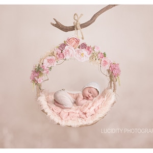 May include: A newborn baby sleeping in a pink and white floral swing. The swing is made of a natural material and is decorated with pink flowers.