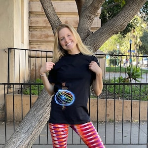 May include: A woman wearing a black t-shirt with a colorful graphic design and tie-dye leggings. The leggings are orange, pink, and purple.