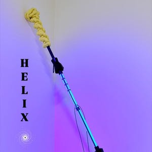 Puede incluir: Una varita Helix negra y amarilla con un centro azul brillante. La varita tiene extremos trenzados amarillos y un mango negro. El texto "HELIX WAND" está impreso verticalmente. Peso: 198 gramos.