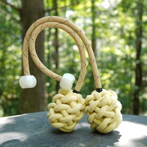 Puede incluir: Dos poi de fuego de cuerda beige con mangos de espuma blanca y detalles negros y rojos en la cuerda.