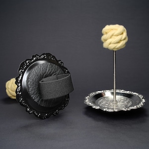 May include: Two black metal candle holders with ornate designs. One holder has a black leather base and a black strap. The other holder has a silver base and a white cotton wick.