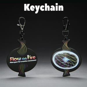 Peut inclure: Porte-clés noir avec un design unique. Il comprend un mousqueton en métal noir et un pendentif avec le texte "Flow on Fire" et le slogan "Flow gear for creative movement". Le pendentif présente des lignes abstraites colorées.