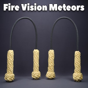 Puede incluir: Dos poi de fuego con el texto "Fire Vision Meteors" en la parte superior. Cuentan con un asa de cuerda negra y cabezas cilíndricas beige hechas de cuerda bien enrollada. El fondo es gris oscuro.