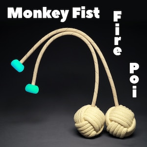May include: A pair of beige monkey fist fire poi with turquoise handles. The poi are tied together with a rope and are suspended in the air.
