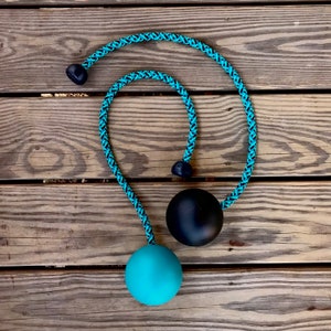 Puede incluir: Un juguete de cuerda turquesa y negra con tres esferas negras y una esfera turquesa. La cuerda está trenzada con un patrón turquesa y negro. El juguete está diseñado para jugar y hacer ejercicio.