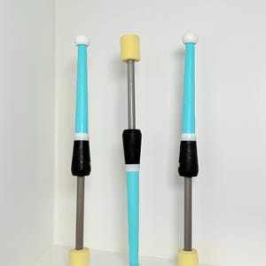 May include: Three juggling clubs with grey shafts, light blue tapered sections, black grips, and white end caps. Two clubs feature yellow textured ends, while the center club has a yellow textured top and a white end cap at the base.
