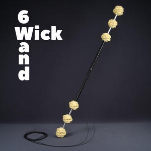 Puede incluir: Una varita de fuego negra con seis bolas de llama amarillas unidas. La varita está sobre una superficie gris oscuro con un cordón negro unido a la varita.