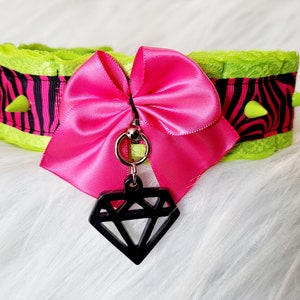 May include: A green and black zebra print choker with a pink satin bow and a black diamond charm.