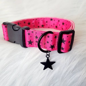 May include: A pink dog collar with black stars and a black star charm. The collar has a black buckle and a black D-ring.
